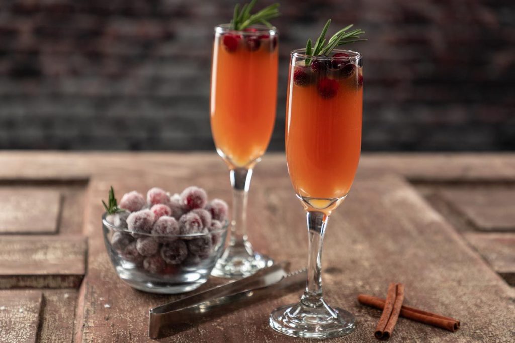 Cranberry, orange, apple cider mimosa in a champagne flute. Garnished with cranberries, cinnamon, and a sprig of rosemary.