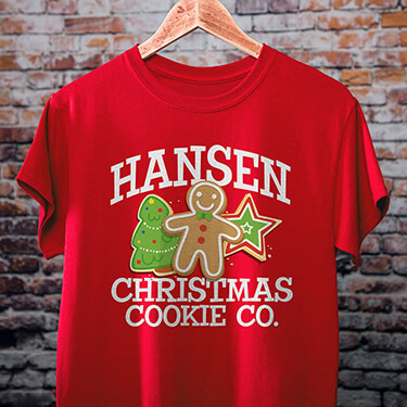 A red Christmas Cookie Company T-shirt with a brick wall in the background