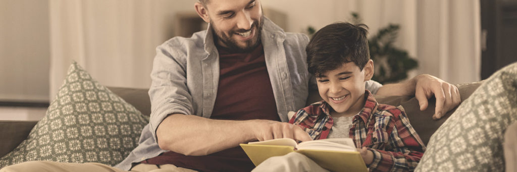 A father reading aloud to his son while sitting on a comfortable couch.